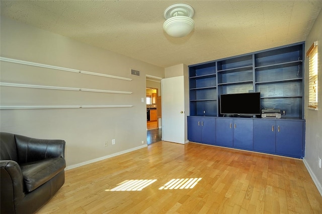 unfurnished living room with built in shelves, light hardwood / wood-style floors, and a textured ceiling