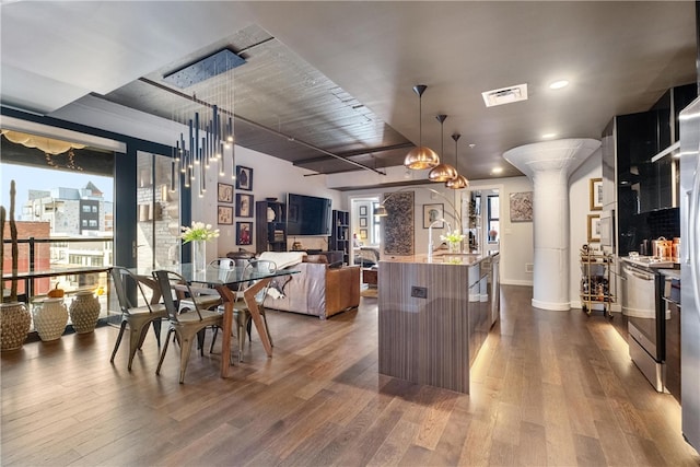 kitchen with stainless steel range, decorative light fixtures, hardwood / wood-style flooring, and a center island with sink