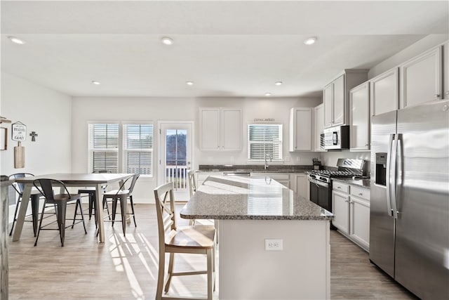 kitchen with sink, light stone counters, light hardwood / wood-style floors, a kitchen island, and appliances with stainless steel finishes