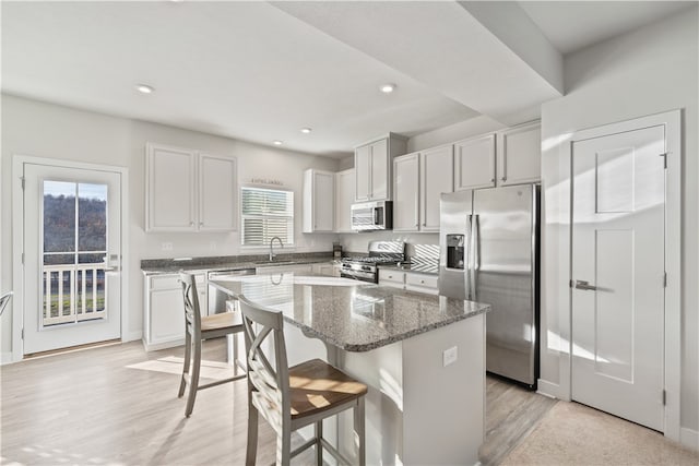 kitchen with white cabinetry, a center island, stainless steel appliances, dark stone countertops, and light wood-type flooring