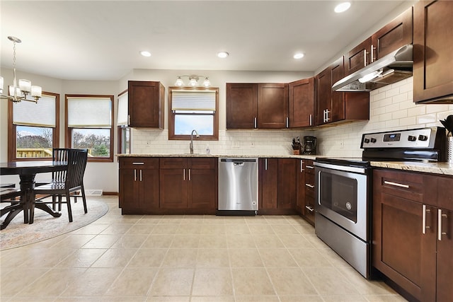 kitchen featuring light stone countertops, hanging light fixtures, a notable chandelier, extractor fan, and appliances with stainless steel finishes