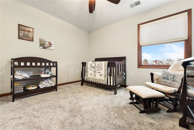 carpeted bedroom featuring ceiling fan and a crib