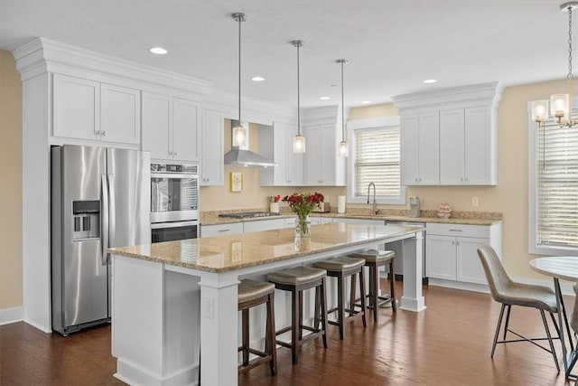 kitchen featuring white cabinets, a center island, stainless steel appliances, and wall chimney range hood