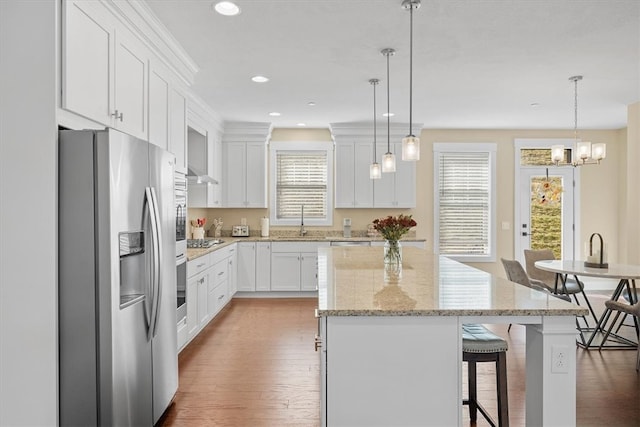 kitchen with white cabinets, appliances with stainless steel finishes, a center island, and decorative light fixtures