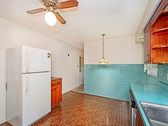 kitchen featuring ceiling fan, sink, hanging light fixtures, white refrigerator, and tile walls