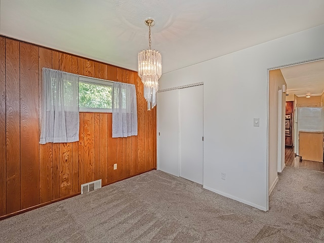 carpeted empty room with wooden walls and an inviting chandelier