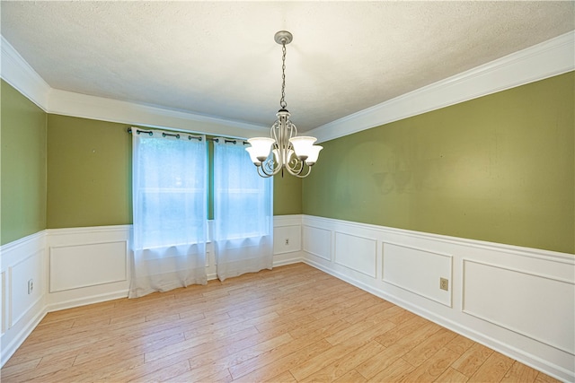 empty room with a textured ceiling, light hardwood / wood-style floors, crown molding, and a chandelier