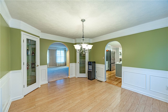 unfurnished dining area featuring crown molding, light hardwood / wood-style flooring, a textured ceiling, and an inviting chandelier