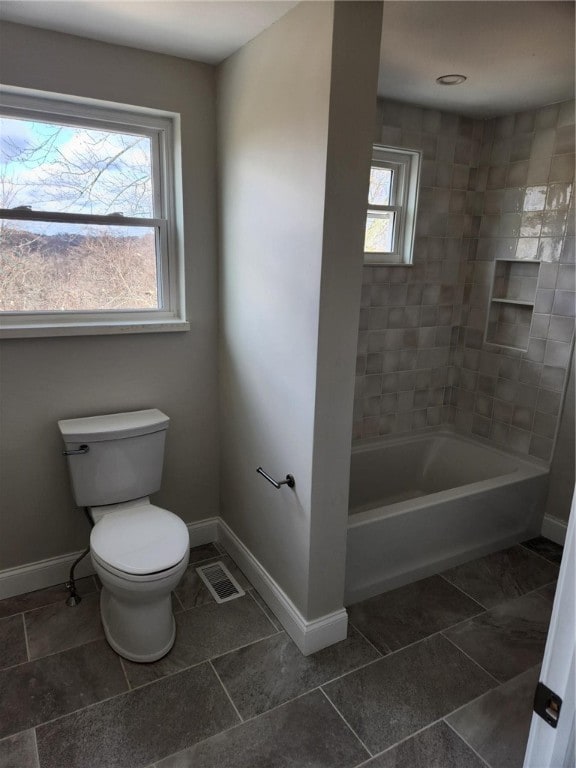 bathroom featuring a wealth of natural light, tiled shower / bath combo, and toilet