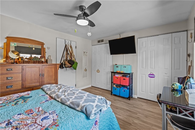 bedroom featuring light hardwood / wood-style floors, ceiling fan, and multiple closets