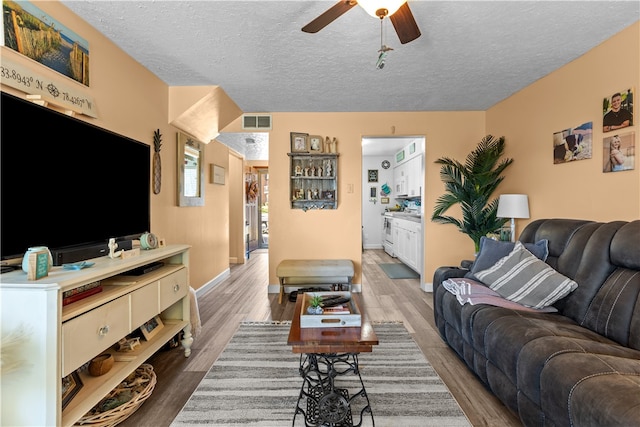 living room featuring hardwood / wood-style flooring, ceiling fan, and a textured ceiling