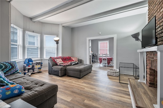 living room featuring beamed ceiling, hardwood / wood-style flooring, and a brick fireplace