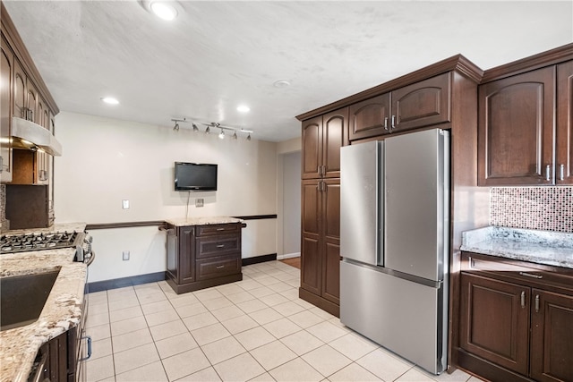 kitchen featuring decorative backsplash, light tile patterned floors, appliances with stainless steel finishes, light stone counters, and dark brown cabinetry