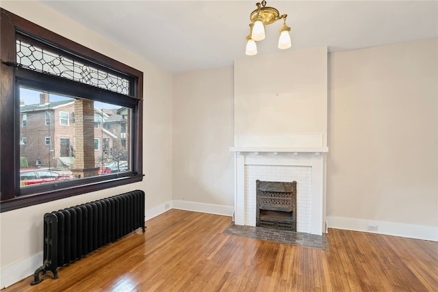 unfurnished living room featuring hardwood / wood-style flooring, a notable chandelier, and radiator