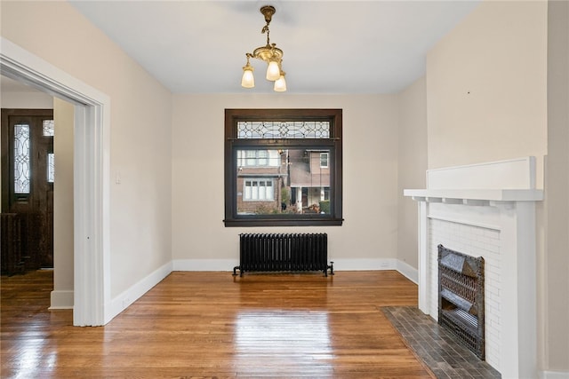 unfurnished living room with a chandelier, radiator heating unit, a fireplace, and wood-type flooring