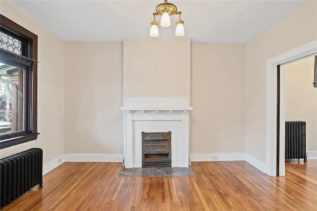 unfurnished living room featuring hardwood / wood-style flooring, radiator heating unit, a fireplace, and an inviting chandelier