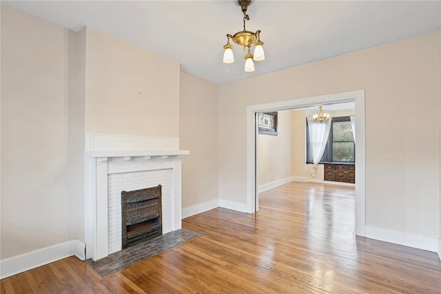 unfurnished living room with a notable chandelier, wood-type flooring, and a brick fireplace