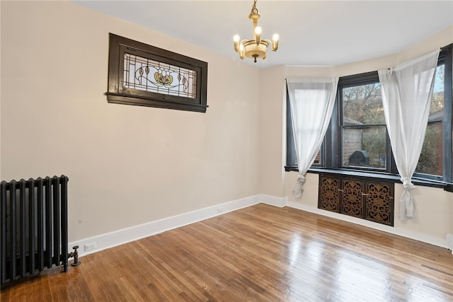 unfurnished room with radiator heating unit, hardwood / wood-style floors, and an inviting chandelier