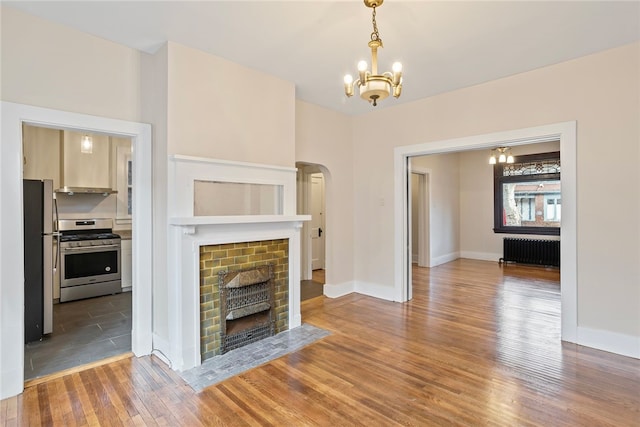 unfurnished living room featuring radiator heating unit, an inviting chandelier, a brick fireplace, and hardwood / wood-style floors