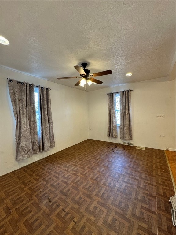 spare room with ceiling fan, dark parquet floors, a healthy amount of sunlight, and a textured ceiling