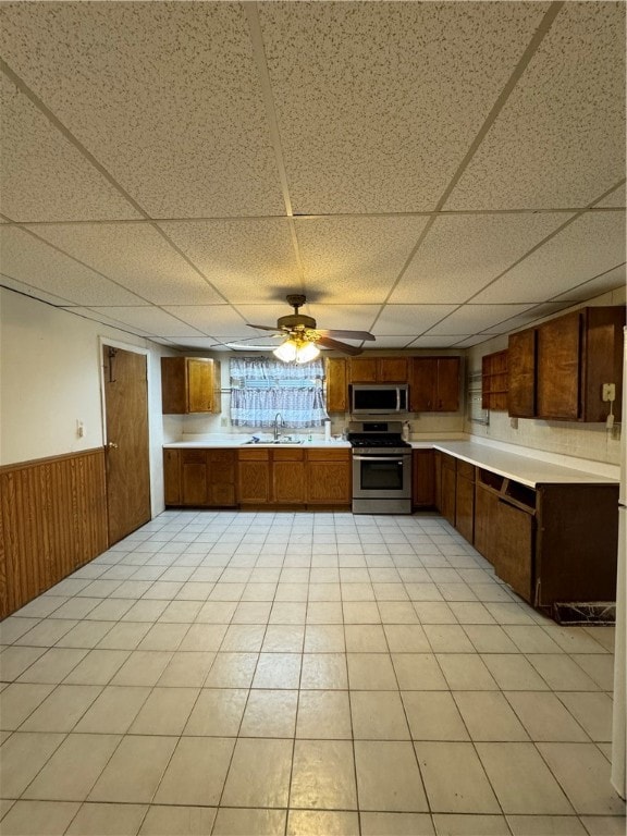 kitchen with a drop ceiling, wood walls, sink, ceiling fan, and stainless steel appliances