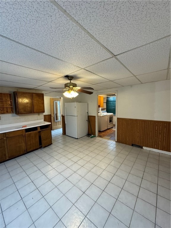 kitchen featuring a drop ceiling, white appliances, ceiling fan, wooden walls, and light tile patterned floors