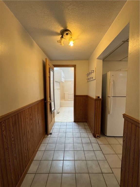 hall featuring wood walls, light tile patterned floors, and a textured ceiling