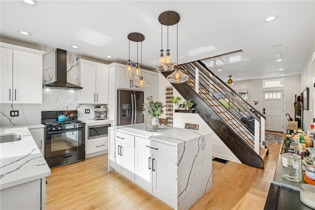 kitchen with a center island, wall chimney exhaust hood, hanging light fixtures, stainless steel appliances, and light wood-type flooring