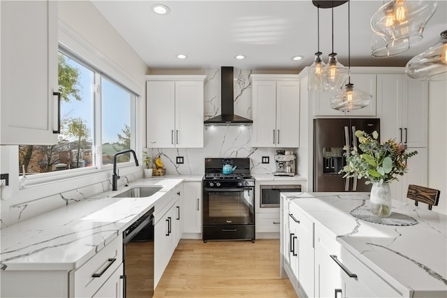 kitchen featuring black appliances, wall chimney range hood, light hardwood / wood-style flooring, decorative light fixtures, and white cabinetry