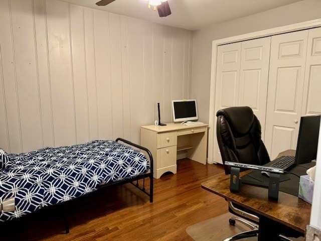 bedroom featuring ceiling fan, dark hardwood / wood-style flooring, wooden walls, and a closet