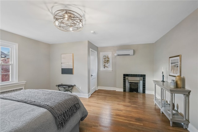 bedroom with a wall mounted air conditioner, wood-type flooring, radiator heating unit, and a tiled fireplace