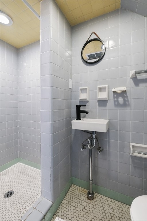 bathroom with a tile shower, sink, tile walls, tile patterned flooring, and toilet