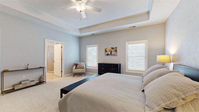 bedroom featuring connected bathroom, light colored carpet, a raised ceiling, and ceiling fan