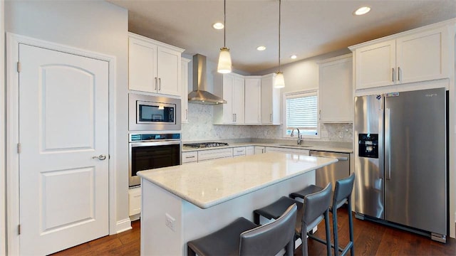 kitchen with wall chimney range hood, sink, hanging light fixtures, a kitchen island, and stainless steel appliances