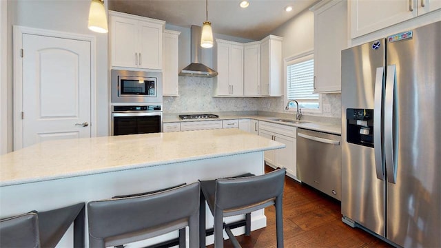 kitchen with appliances with stainless steel finishes, wall chimney exhaust hood, sink, pendant lighting, and white cabinets