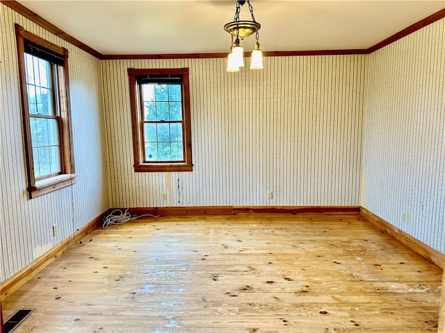 empty room with light wood-type flooring, ornamental molding, and an inviting chandelier