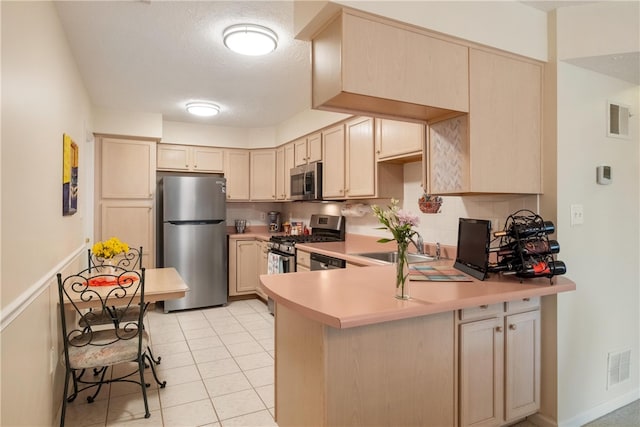 kitchen featuring light tile patterned floors, a textured ceiling, light brown cabinetry, appliances with stainless steel finishes, and kitchen peninsula