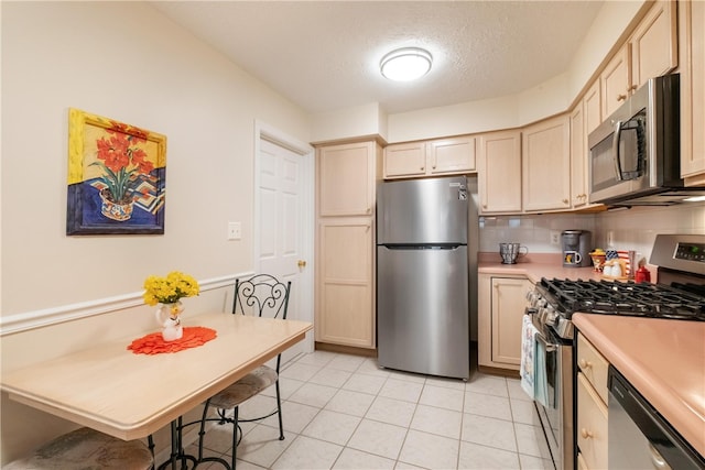 kitchen with decorative backsplash, a textured ceiling, stainless steel appliances, light brown cabinets, and light tile patterned floors