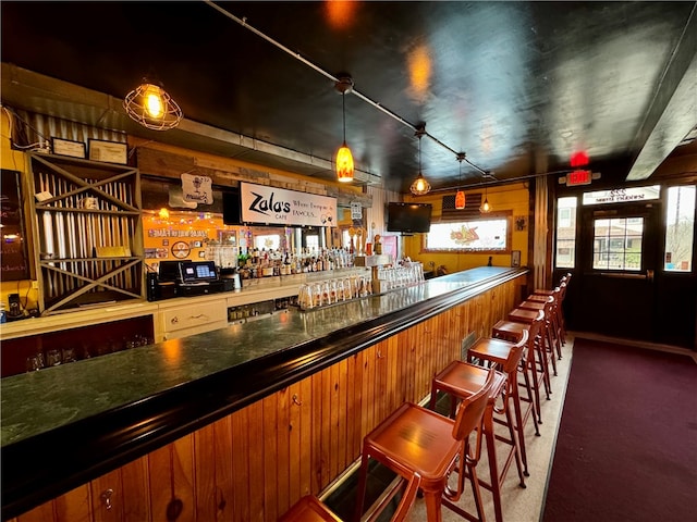 bar featuring wood walls, dark carpet, and hanging light fixtures