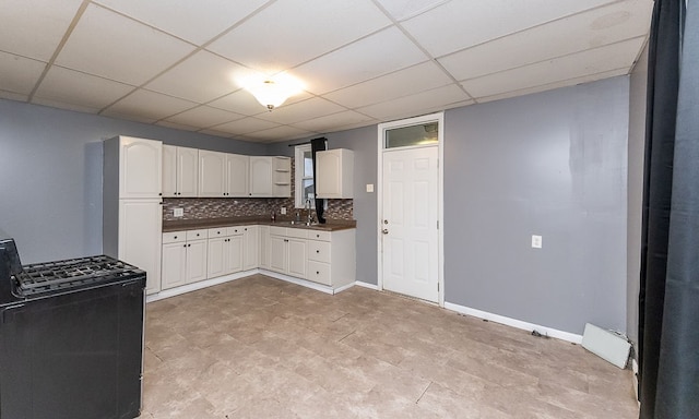 kitchen featuring backsplash, a drop ceiling, black range oven, sink, and white cabinets