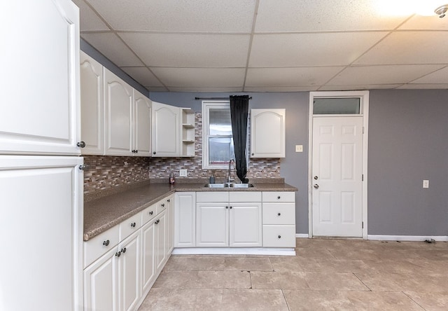 kitchen featuring a paneled ceiling, white cabinets, sink, decorative backsplash, and light tile patterned floors