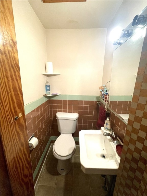 bathroom with tile patterned flooring, toilet, sink, and tile walls