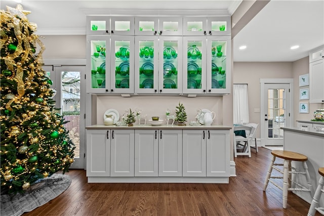 bar featuring dark hardwood / wood-style flooring, white cabinetry, and crown molding