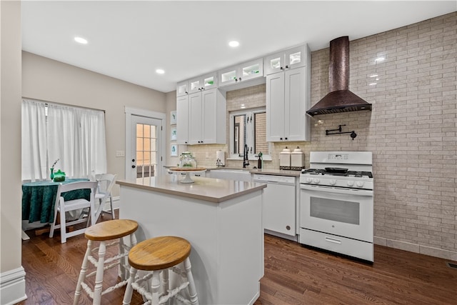 kitchen featuring dark hardwood / wood-style flooring, white appliances, a kitchen island, wall chimney range hood, and white cabinetry