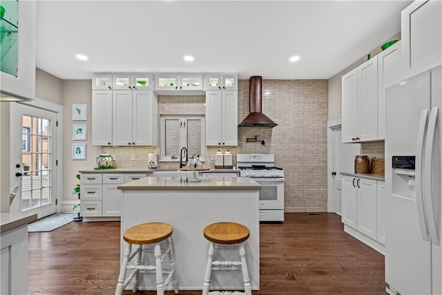 kitchen featuring a breakfast bar, a center island, white appliances, wall chimney exhaust hood, and white cabinetry