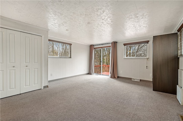 unfurnished bedroom featuring light carpet, access to exterior, a closet, and wooden walls