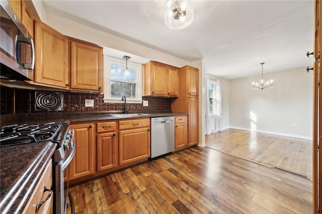 kitchen featuring appliances with stainless steel finishes, dark hardwood / wood-style flooring, sink, pendant lighting, and an inviting chandelier