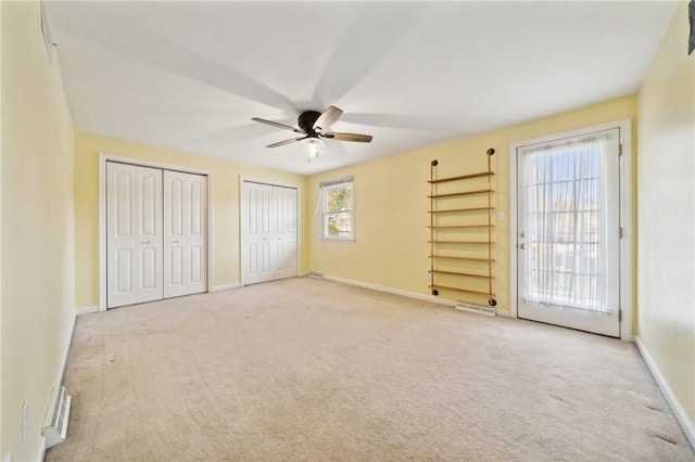 unfurnished bedroom featuring ceiling fan, light carpet, and two closets