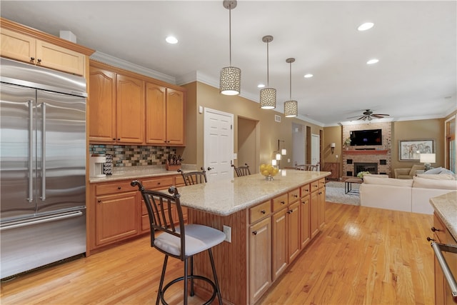 kitchen with stainless steel built in refrigerator, ceiling fan, a fireplace, light hardwood / wood-style floors, and hanging light fixtures