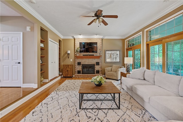 living room with built in shelves, ceiling fan, a brick fireplace, light hardwood / wood-style floors, and ornamental molding